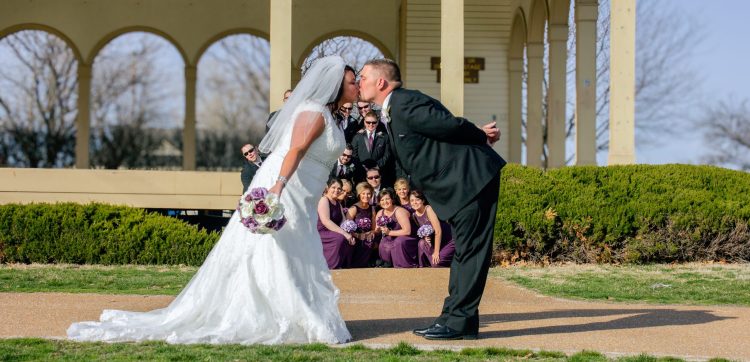 Bride and Groom kissing with wedding party behind them