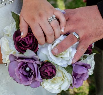 Bride and Grooms hands on bouquet with purple flowers