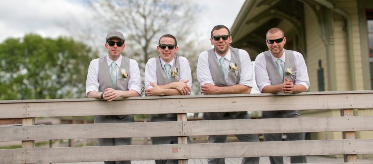 groom and groomsmen leaning on a rail