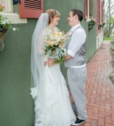 bride and groom leaning on wall smiling at each other