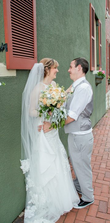 bride and groom leaning on wall smiling at each other
