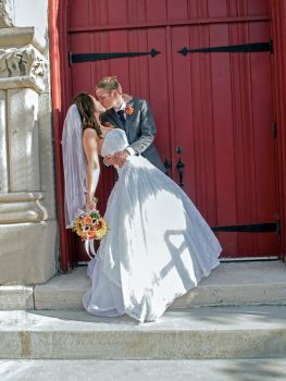 groom dipping bride and kissing at doors to the church